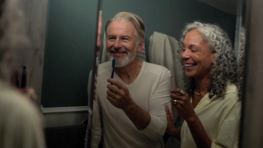 Two people brushing their teeth in front of a mirror