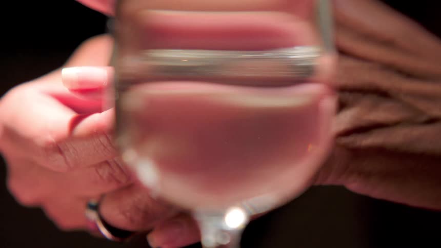 This is a video of a hand presumably female holding a diamond ring near the rim of a wine glassthe focus shifts between the sparkling ring and the liquid possibly wine or water inside the glass with the hand in the background