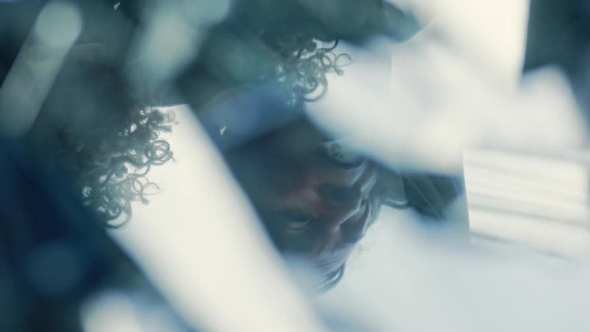 This video is a closeup abstract shot of a persons face possibly a woman looking downwardthe image is heavily distorted and fragmented by reflections through what appears to be glass or crystalline objects creating a moody fragmented visual eff