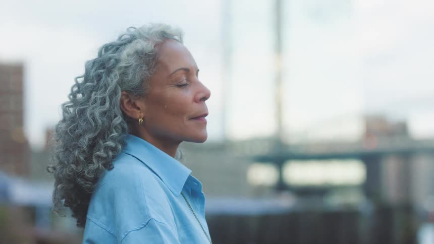 Older woman leans against a rail on the waterfront and takes a deep breath