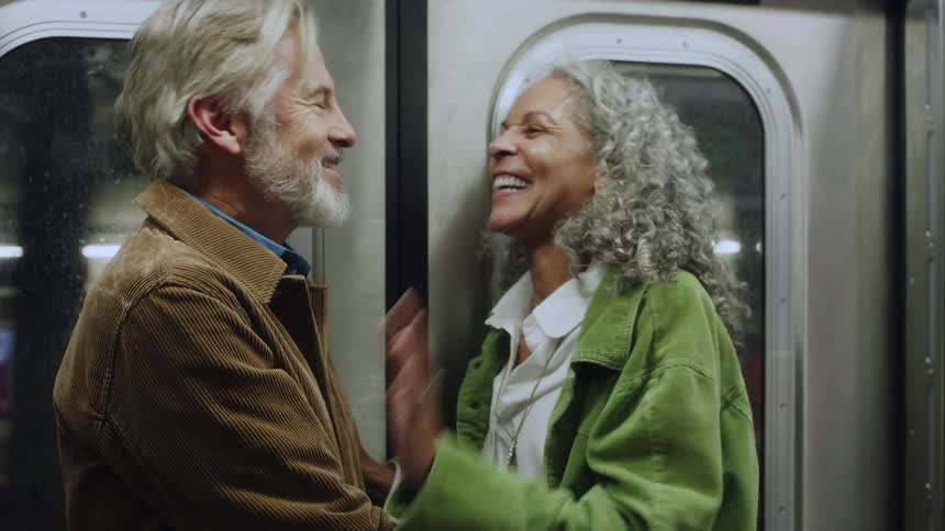 A smiling middle aged couple lovingly embraces while standing on a moving subway train