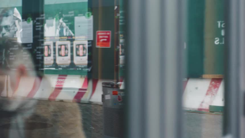 An older female walking outside walks past a shop where she looks sad as she looks at an older man seated indoors