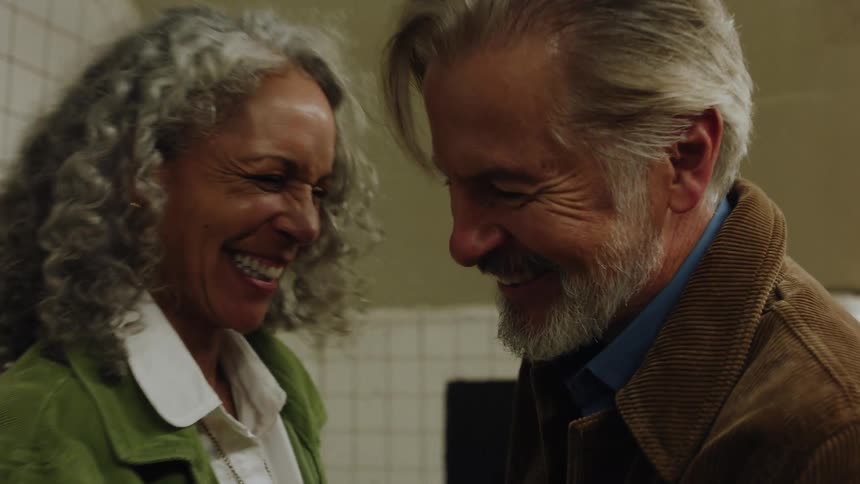 A silverhaired couple shares a warm embrace and joyful laughter on a subway platform holding each other tight as they reconnect in the dim station light