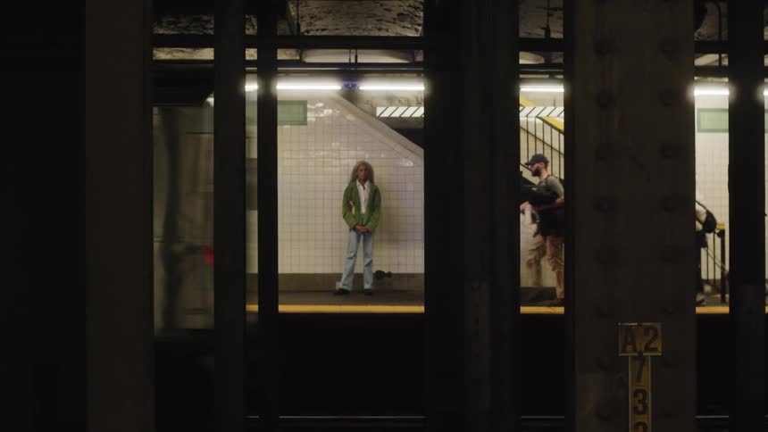 Train in motion passes in front of columns while a female figure stands still in the background