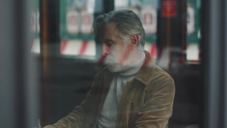 Man writes in a notebook in a coffee shop while a woman watches from outside