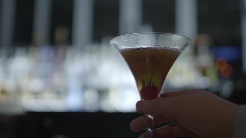 Person picks up cocktail glass in bar