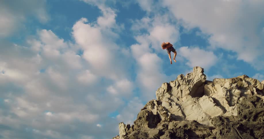 Person jumps from the rocks into the sea under a partly cloudy sky