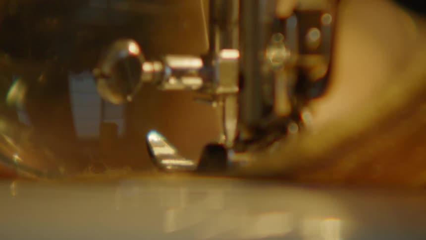 Person using a magnifying glass operates a sewing machine