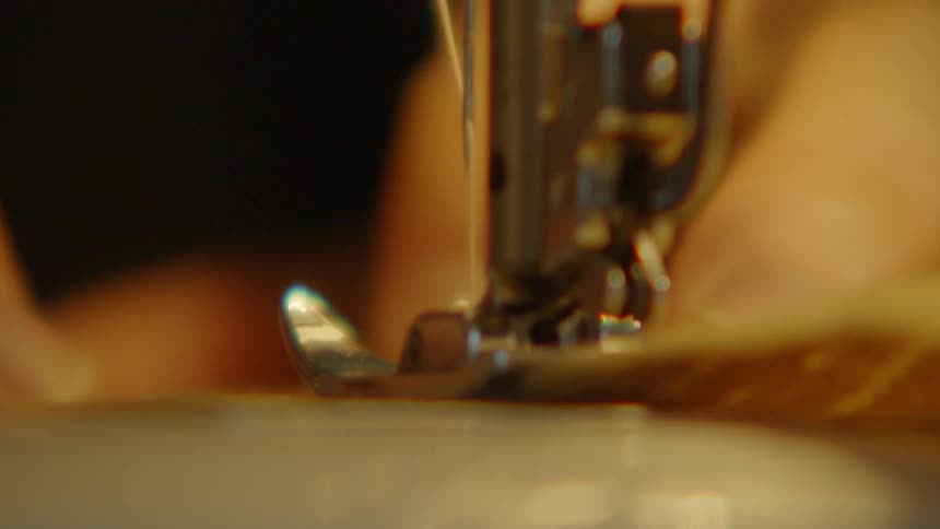 A person stitches fabric with a sewing machine the area brightly illuminated by a strong light