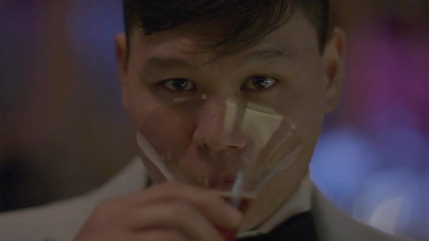 Asian man takes a drink out of a large glass