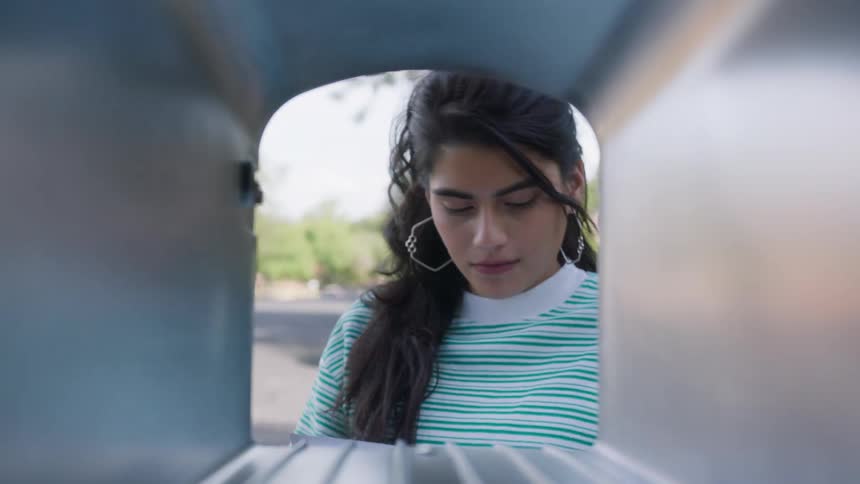 Person in striped shirt retrieves mail from inside mailbox