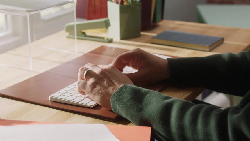 Person typing on white keyboard on wooden desk with stationery and books around