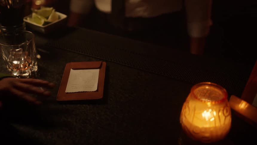 A customer at a counter with a candle is paying for a bill with cash to a worker no faces can be seen