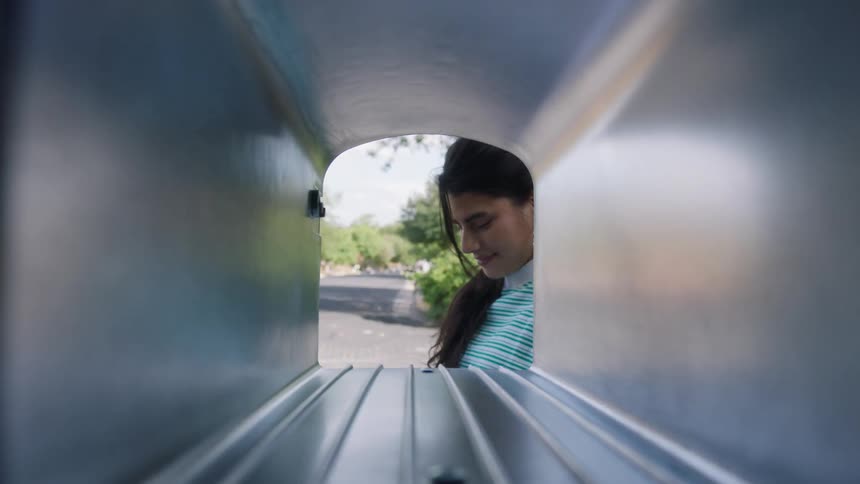 The video shows the interior perspective of a mailbox looking outward a young woman with long dark hair is seen leaning in to check for mail and then closes the box