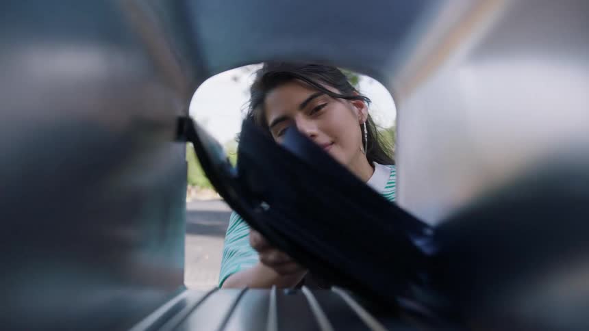 Viewed from inside a mailbox a young woman opens the door sorts through a stack of mail and smiles as she pulls out a single white envelope