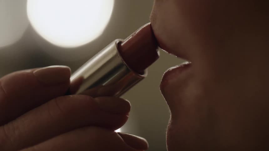 A woman applies lipstick to her lips
