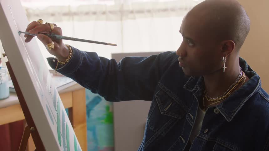 A man in a denim jacket paints on a canvas
