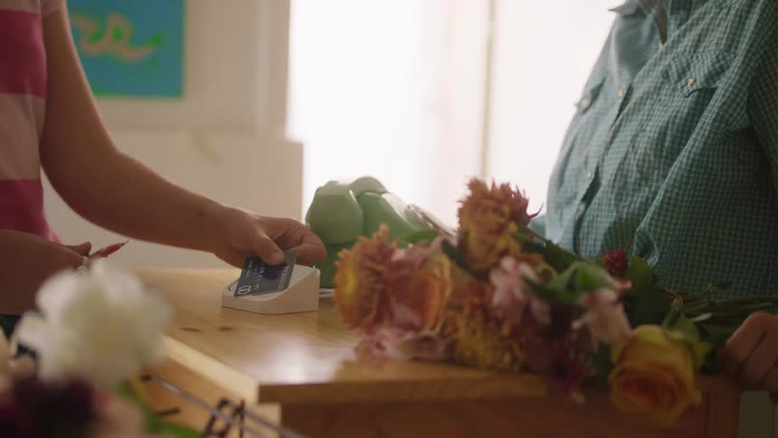 Customer buys a bouquet of flowers in a floral shop as the cashier processes their credit card