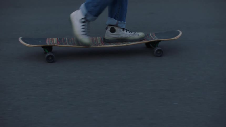 Legs of person wearing jeans and white sneakers skateboarding on asphalt outdoors