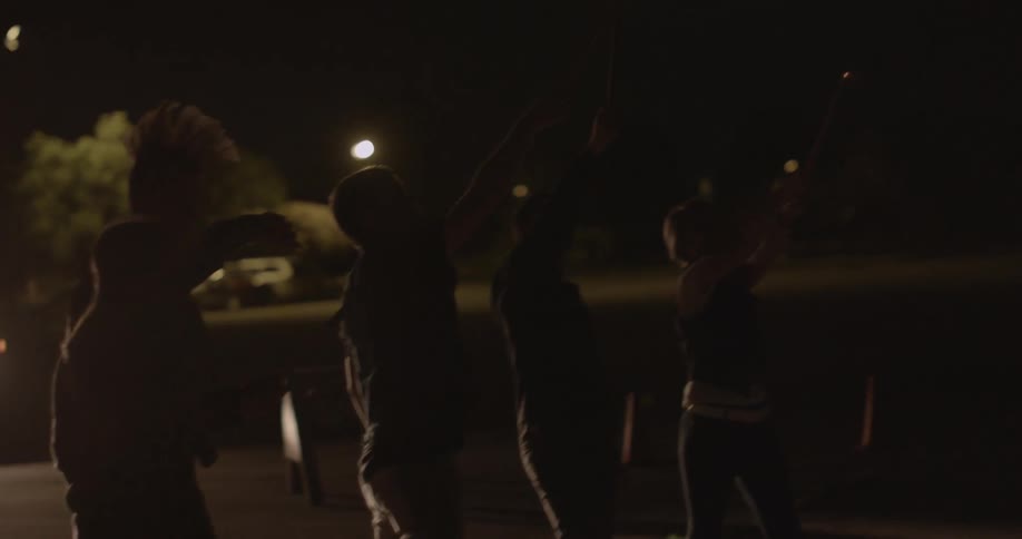 Teenagers light and hold sparklers up in the night sky