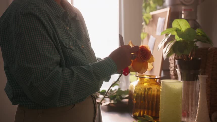 A florist trims the stem of an orange flower in a modern flower shop
