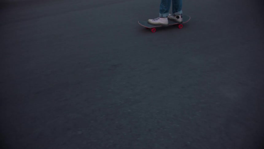 Person glides on a skateboard across the asphalt wearing white sneakers and jeans