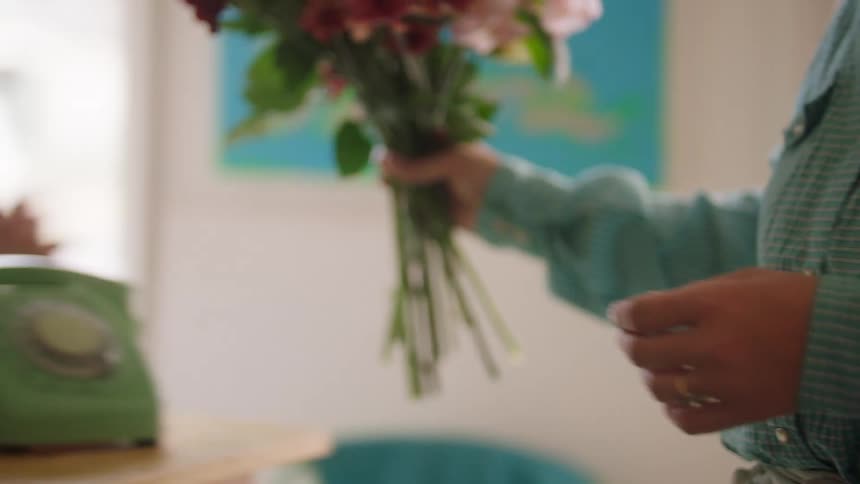 Person in pink striped shirt hands colorful bouquet in front of blue decorated wall