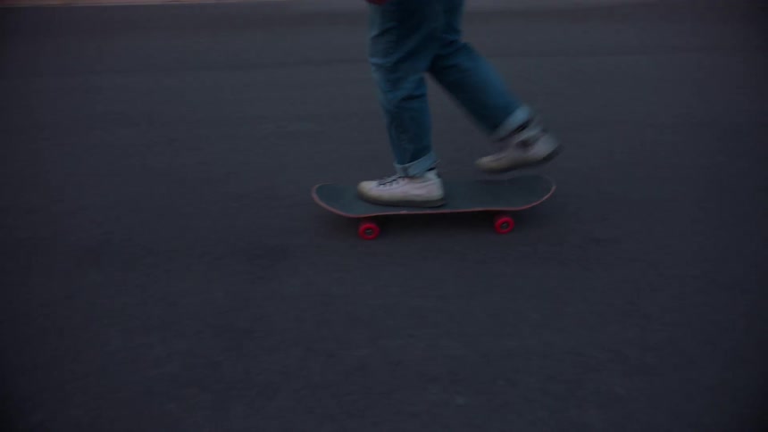 A persons legs are shown using and riding on a skateboard on a road at dusk
