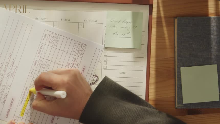 A closeup of hands highlighting information on paperwork at a desk