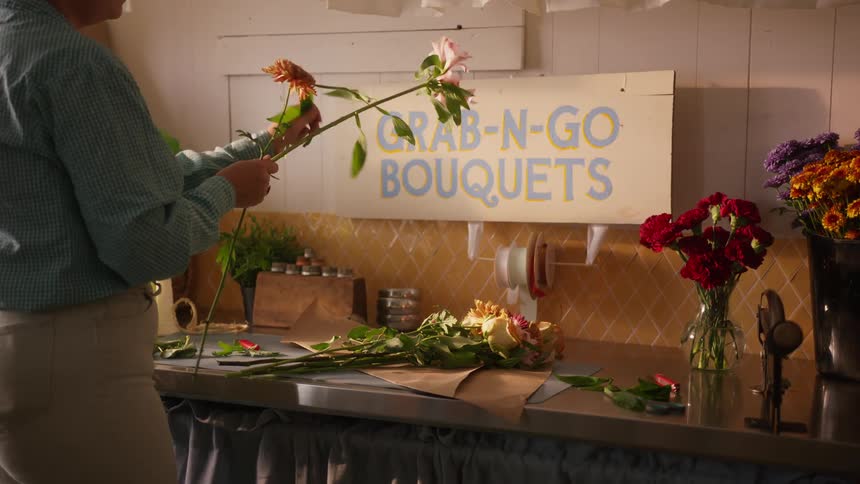 A person is separating some flowers on a table with a sign above them