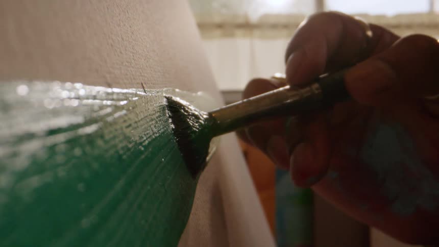 The bristles of a paintbrush press against a textured white canvas slowly dragging a trail of vibrant green paint across the surface