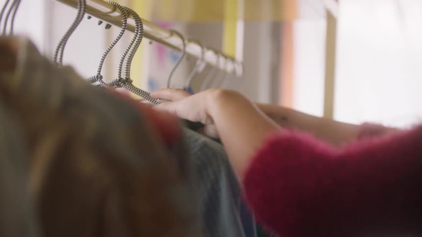 Hand arranges clothes hanging on metal hangers