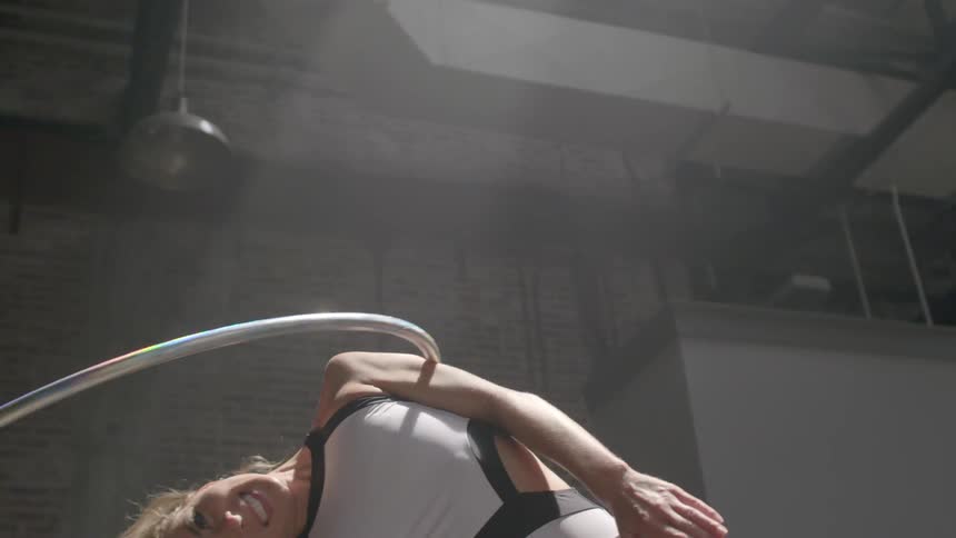 A woman in a dance uniform twirls a hula hoop up her body