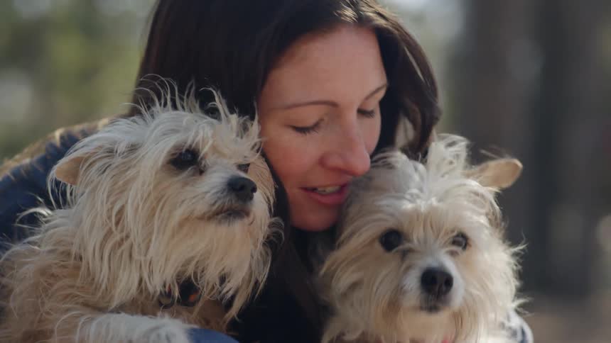 A woman hugs and kisses two small dogs