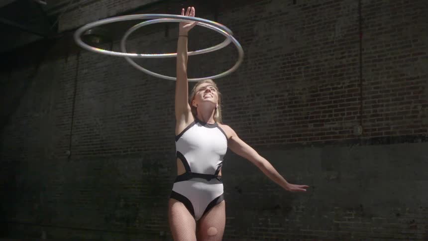 A woman twirls two hula hoops on one arm