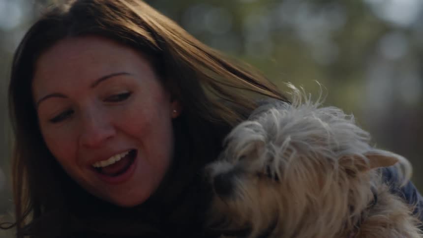 A woman laughs as a dog licks her face