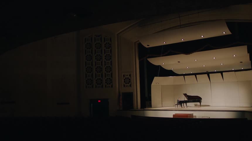 A person is sitting at a piano on stage
