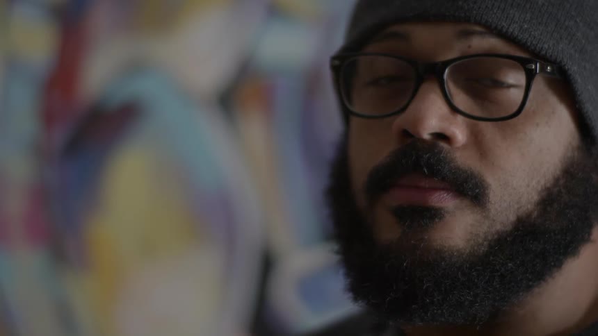 A man in glasses stands in front of a painting