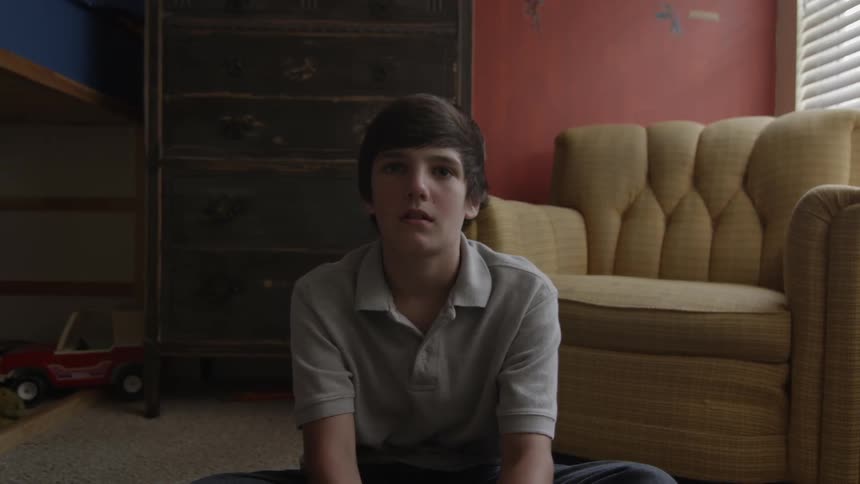 A boy sits on a floor and stares forward