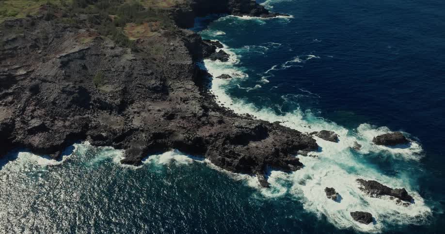 Dark volcanic rock formations on coastline with crashing waves and deep blue ocean in the background