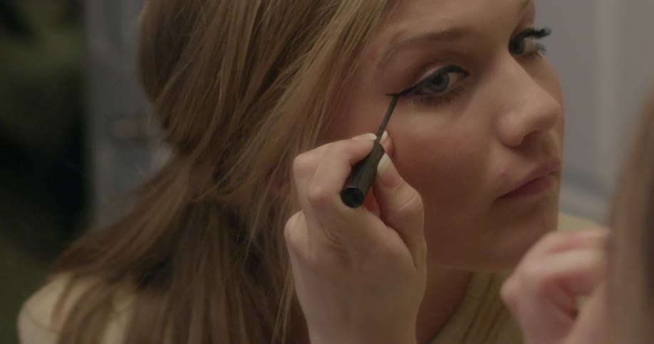 Woman looks in a mirror to put on eye makeup