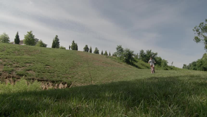A person rides a bicycle on a grassy hill