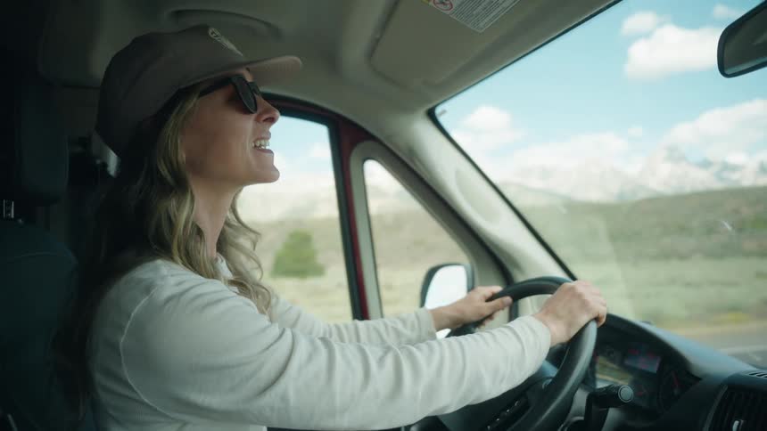 Woman drives while smiling and looking at the landscape through the vehicle window