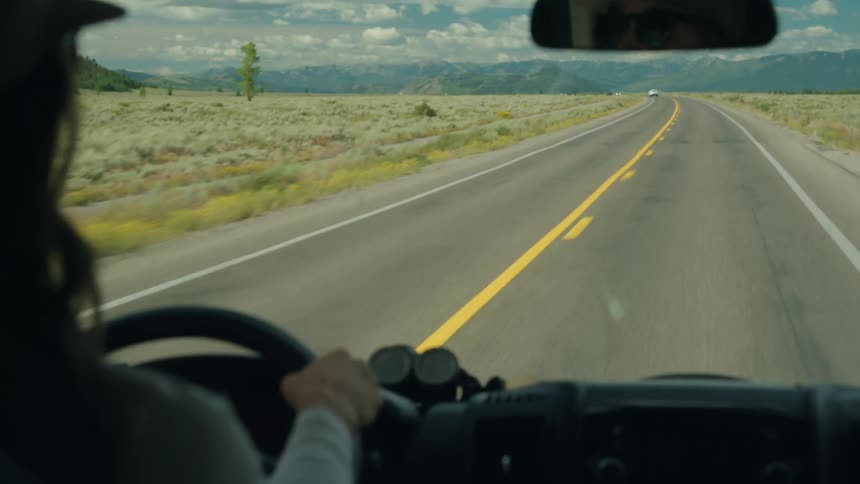 Man driving on a rural highway with mountains in the distance