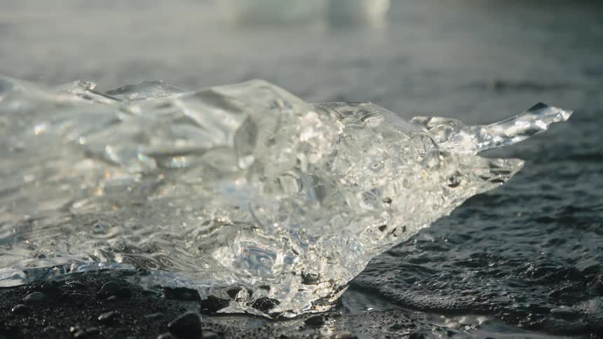 Transparent ice on dark wet surface with blurred water in the background