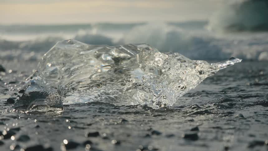 Transparent ice chunk floating in dark water with waves in background