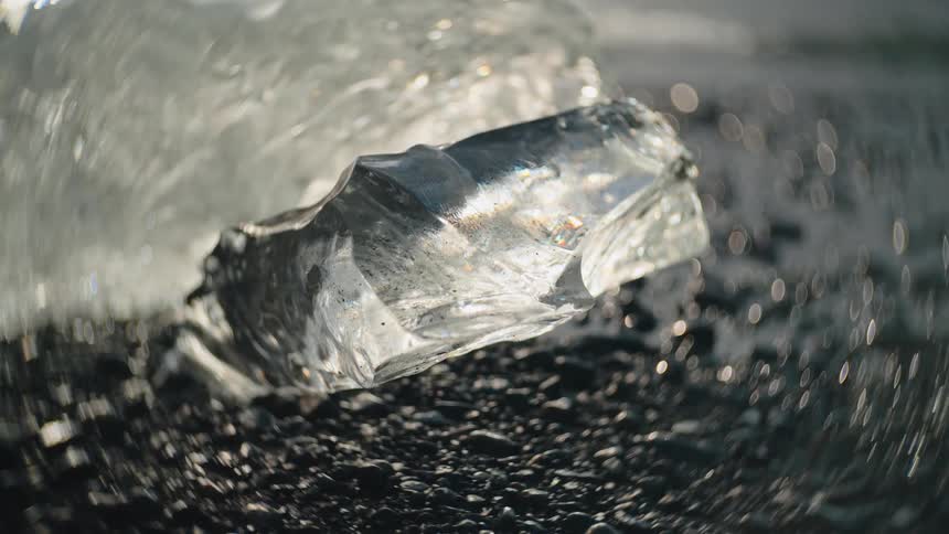 Transparent ice chunk on dark pebbled surface