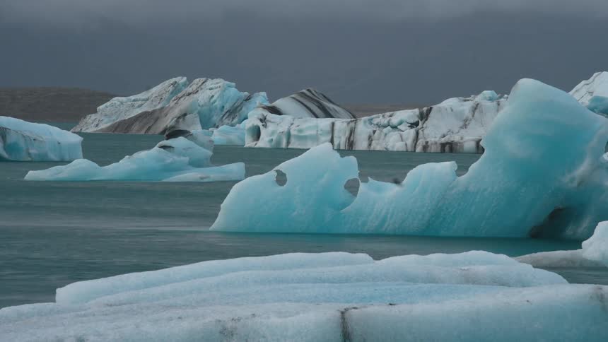 Irregular icebergs floating in blue water under cloudy sky