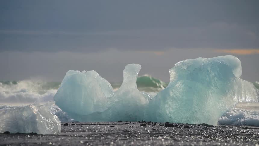 The sun shines and rain falls as icebergs melt along the coast and waves roll into shore