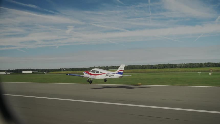 Singleengine plane with red and blue details landing on a runway surrounded by fields trees and a sky with trails
